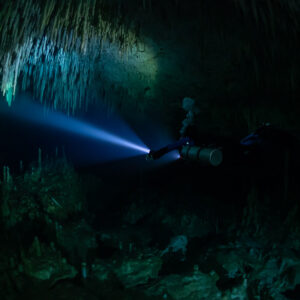 Sidemount diver far in a large room lighting stalactite curtains, Quintana Roo, Mexico