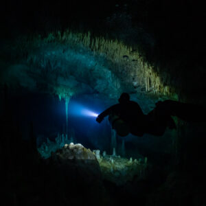 Diver silhouette lighting a stalactite dome in a dark room, Quintana Roo, Mexico