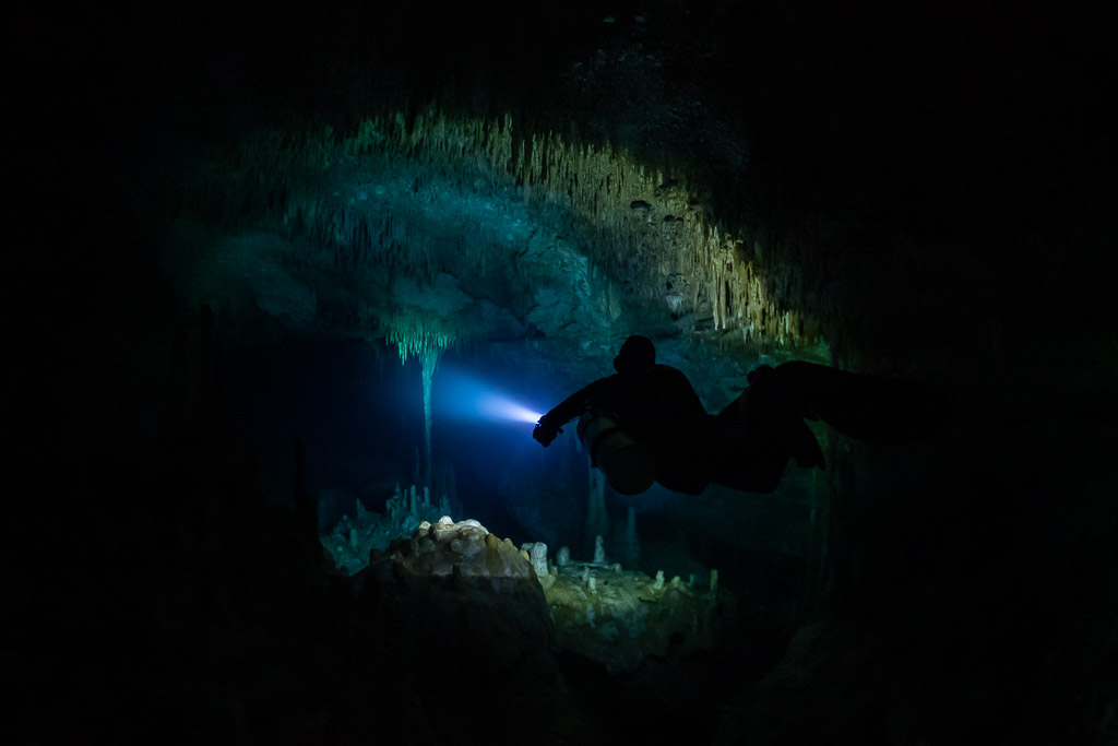 Diver silhouette lighting a stalactite dome in a dark room, Quintana Roo, Mexico