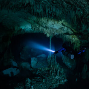 Sidemount diver lighting a low archway with stalactites, Quintana Roo, Mexico