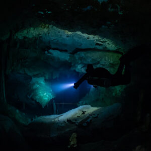 Sidemount diver in an oval cave window lighting the floor beyond, Quintana Roo, Mexico