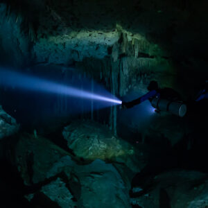 Sidemount diver beaming a long torch over boulders and columns, Quintana Roo, Mexico