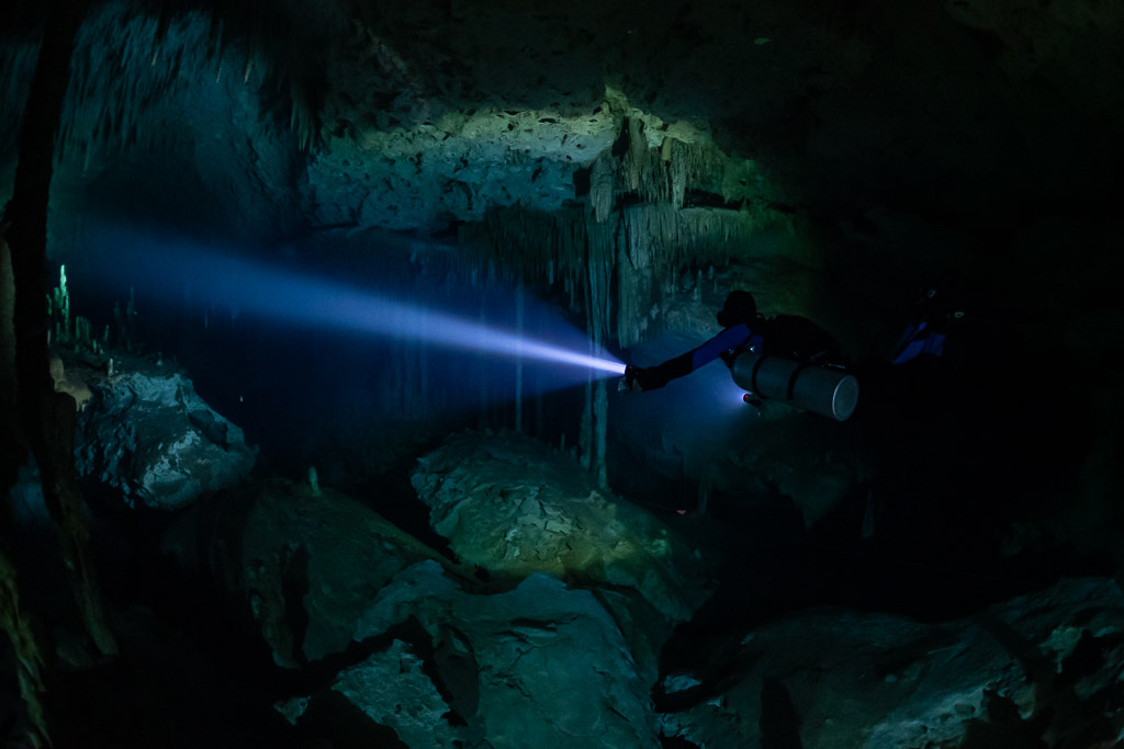 Sidemount diver beaming a long torch over boulders and columns, Quintana Roo, Mexico