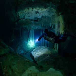 Sidemount diver lighting a green glow between stalactites, Quintana Roo, Mexico