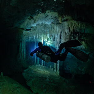Sidemount diver descending past stalactite curtains, torch forward, Quintana Roo, Mexico