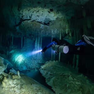 Sidemount diver lighting a green cave room above pale boulders, Quintana Roo, Mexico