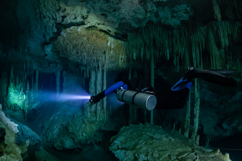 Sidemount diver with blue fins under a decorated ceiling, torch beam, Quintana Roo, Mexico