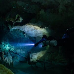 Sidemount diver lighting a cave passage beyond a pale rock ledge, Quintana Roo, Mexico