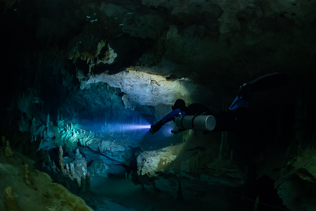 Sidemount diver lighting a cave passage beyond a pale rock ledge, Quintana Roo, Mexico