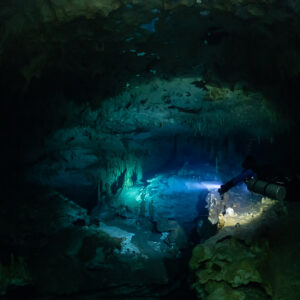 Sidemount diver lighting a turquoise passage under a dark ceiling, Quintana Roo, Mexico