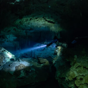 Sidemount diver lighting boulders in a dark cave room, wide view, Quintana Roo, Mexico