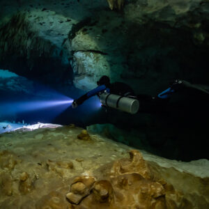 Sidemount diver lighting a passage above an ochre rock slab, Quintana Roo, Mexico