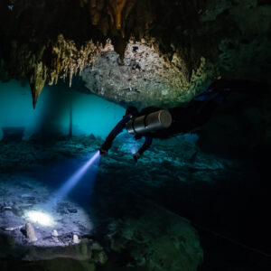 Sidemount diver lighting the floor below a stalactite-hung ceiling, Quintana Roo, Mexico
