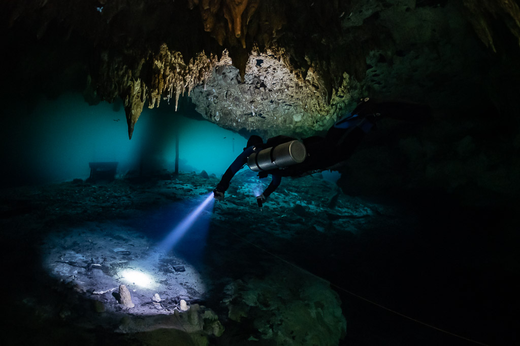Sidemount diver lighting the floor below a stalactite-hung ceiling, Quintana Roo, Mexico
