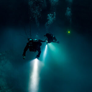 Two technical divers with torches descending in a deep blue cenote, Quintana Roo, Mexico