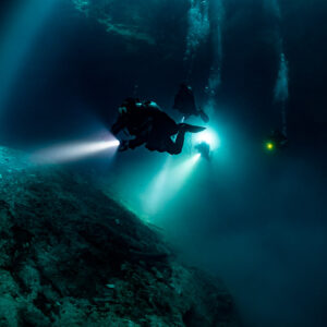 Divers with torches over a rock mound in sunbeams of a deep cenote, Quintana Roo, Mexico