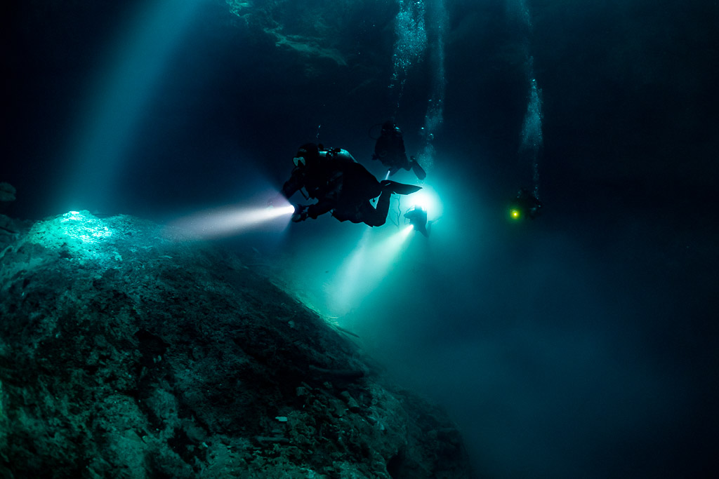 Divers with torches over a rock mound in sunbeams of a deep cenote, Quintana Roo, Mexico
