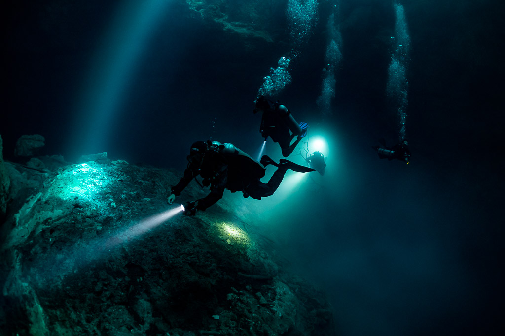 Divers crossing sunbeams above a rock mound with bubble trails, Quintana Roo, Mexico