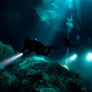 Diver lighting a rock mound, other divers glowing in the blue beyond, Quintana Roo, Mexico