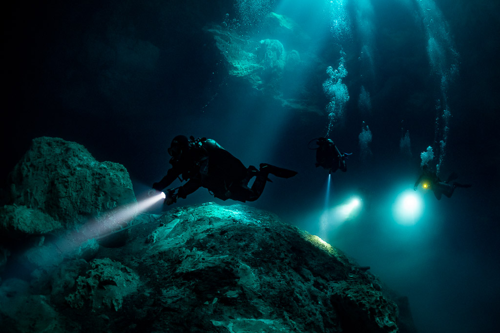 Diver lighting a rock mound, other divers glowing in the blue beyond, Quintana Roo, Mexico