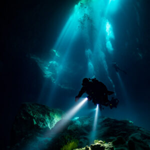 Vue verticale d’un plongeur sous des rais de lumière dans un cénote profond, Quintana Roo, Mexique