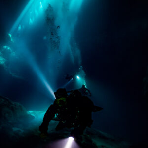 Vertical silhouette of a diver on a rock pile beneath light shafts, Quintana Roo, Mexico