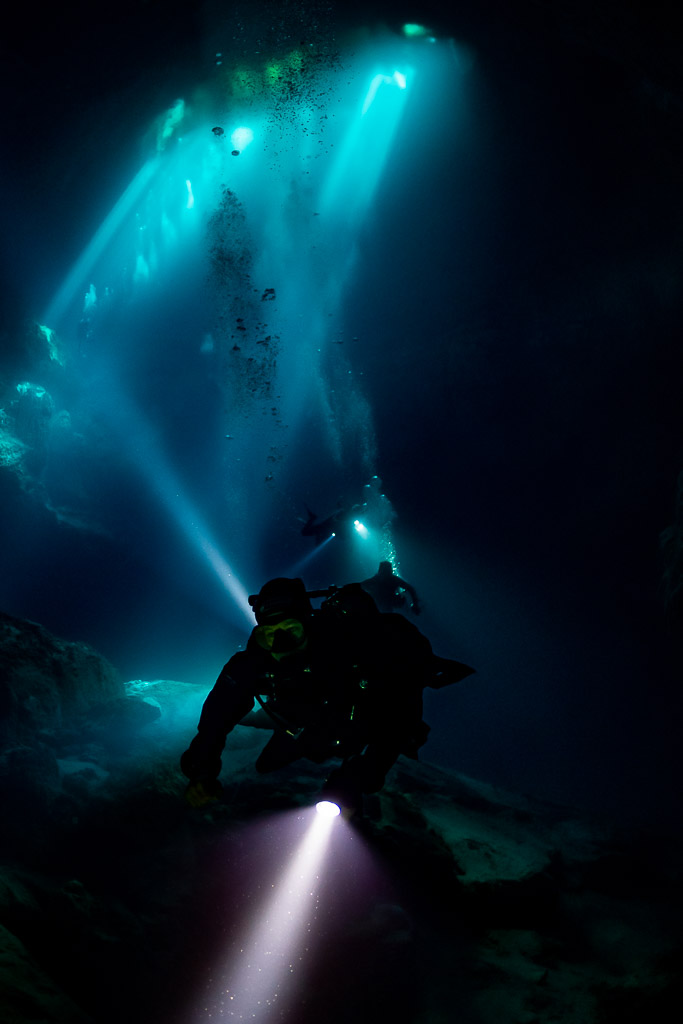 Vertical silhouette of a diver on a rock pile beneath light shafts, Quintana Roo, Mexico
