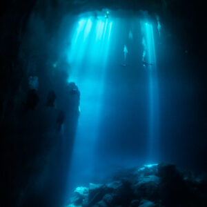 Vertical shafts of sunlight piercing the dark water of a cenote cavern, Quintana Roo, Mexico