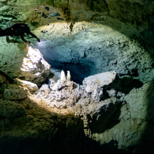 Cave diver silhouetted above a sunlit chamber of white speleothems, Quintana Roo, Mexico