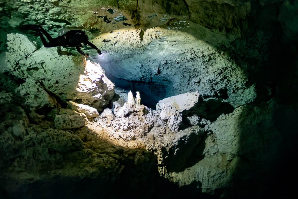 Cave diver silhouetted above a sunlit chamber of white speleothems, Quintana Roo, Mexico