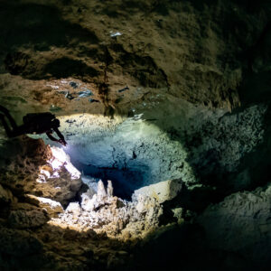Diver hovering over a sunlit pool of stalagmites in a cenote cavern, Quintana Roo, Mexico