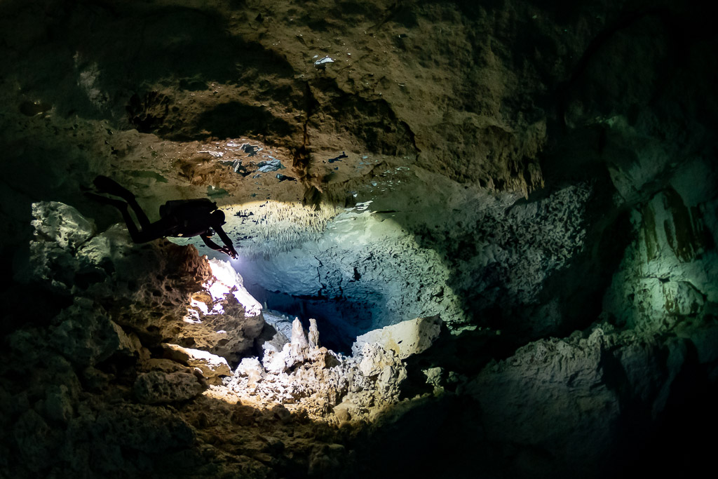 Diver hovering over a sunlit pool of stalagmites in a cenote cavern, Quintana Roo, Mexico