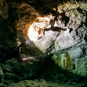 Two cave divers with torches entering a golden sunlit cavern opening, Quintana Roo, Mexico
