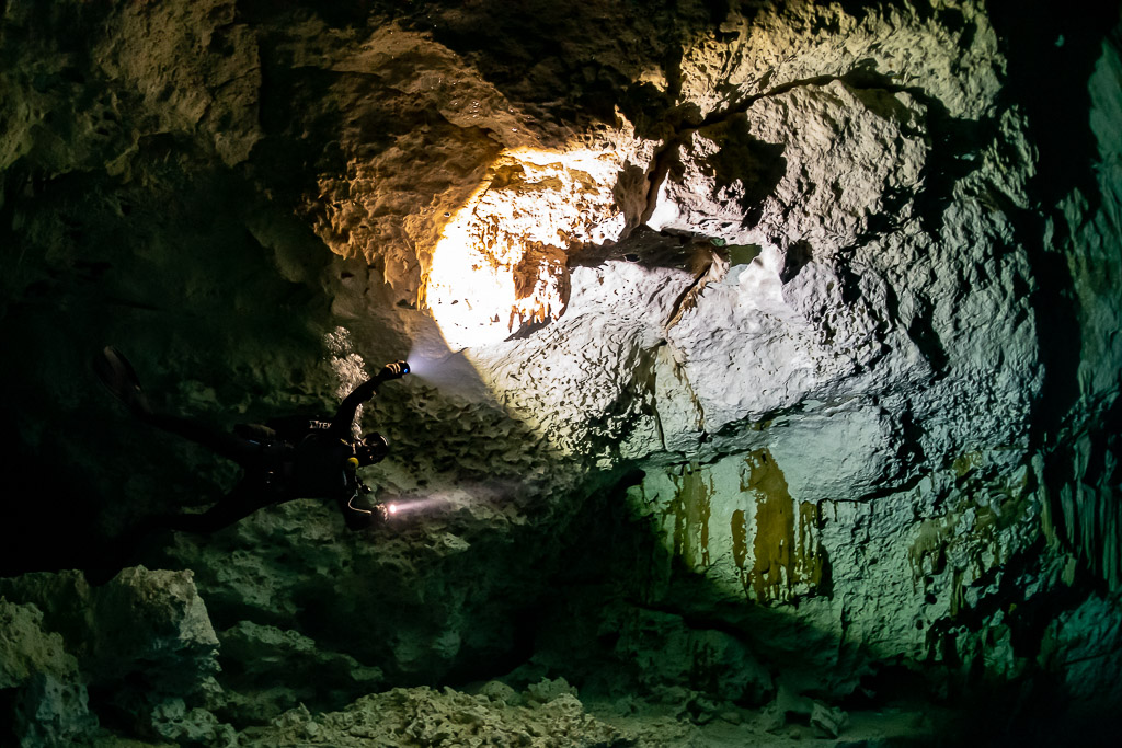 Two cave divers with torches entering a golden sunlit cavern opening, Quintana Roo, Mexico