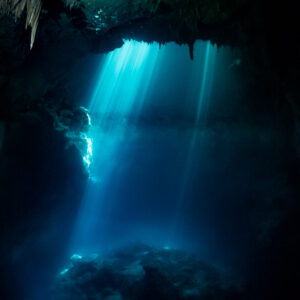 Blue light beams falling into a cenote with stalactites framing the top, Quintana Roo, Mexico