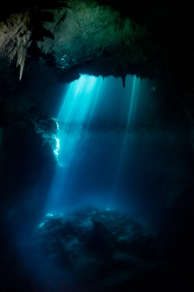 Blue light beams falling into a cenote with stalactites framing the top, Quintana Roo, Mexico