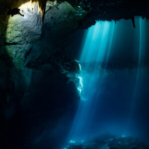 Cenote light beams with a distant diver's torch glowing under the ceiling, Quintana Roo, Mexico