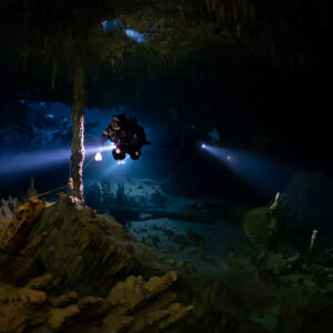 Cave diver lighting a vast chamber behind an ochre stalagmite mound, Quintana Roo, Mexico