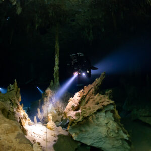 Cave diver behind tall stalagmites on an ochre limestone ridge, Quintana Roo, Mexico