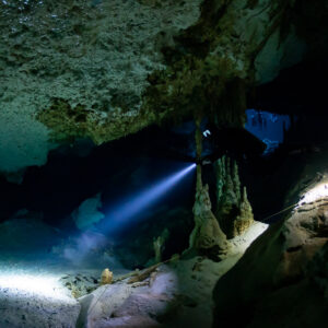 Diver's torch lighting a stalagmite cluster on a pale sandy cave floor, Quintana Roo, Mexico