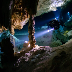 Plongeur spéléo près d’une colonne et de draperies de stalactites sous une lumière chaude, Quintana Roo, Mexique
