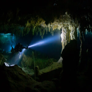 Cave diver beneath a fringe of stalactites with a bright torch beam, Quintana Roo, Mexico