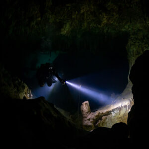 Small cave diver figure lighting a dark chamber with a single beam, Quintana Roo, Mexico
