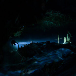 Distant diver torch lighting stalagmites in a very dark cave passage, Quintana Roo, Mexico