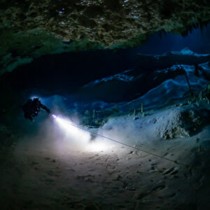 Cave diver lighting a white sandy floor along a guideline in a low passage, Quintana Roo, Mexico