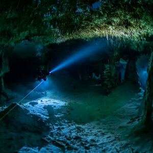 Cave diver shining a torch onto a green-tinted chamber floor, Quintana Roo, Mexico