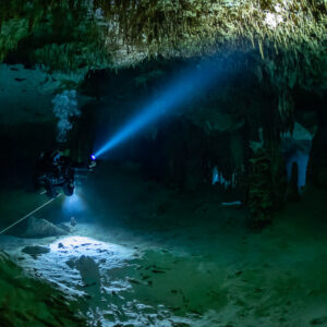 Cave diver with a diagonal torch beam in a wide green chamber, Quintana Roo, Mexico