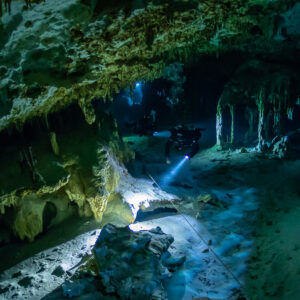 Distant cave diver among pillars beyond an overhanging limestone ledge, Quintana Roo, Mexico