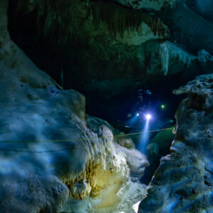 Cave diver approaching through a restriction between sculpted limestone, Quintana Roo, Mexico