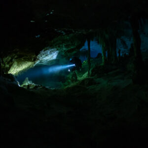 Faint torch beam in a dark low cave chamber with distant formations, Quintana Roo, Mexico
